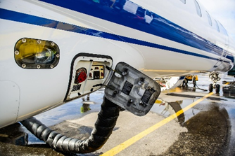 Service panel on a small commercial jet with a connected hose and ground crew in the background on the tarmac